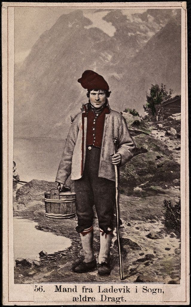 Vintage postcard of a man in traditional clothing standing in a rural landscape.